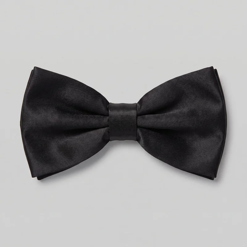 A complete black satin bow tie is shown as a standalone product from the front. It has a symmetrical butterfly silhouette, wide flared folded wings, gathered pinched folds toward the center, and a smooth rectangular center wrap band holding the shape. The outer edges are squared with softly curved top and bottom contours, and layered folded edges are visible at the ends.