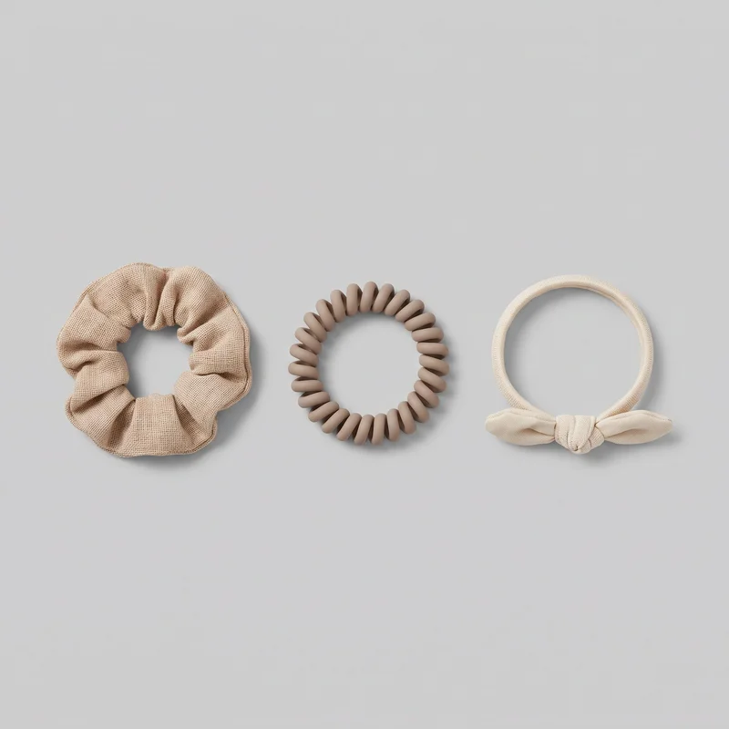 Three separate circular hair accessories are arranged side by side: a gathered scrunchie with ruched volume and seamed edging, a segmented spiral coil hair tie with repeating rounded rib-like sections, and a smooth wrapped elastic loop finished with a tied bow and central knot. No logos, prints, patches, embroidery, or additional embellishments are visible.