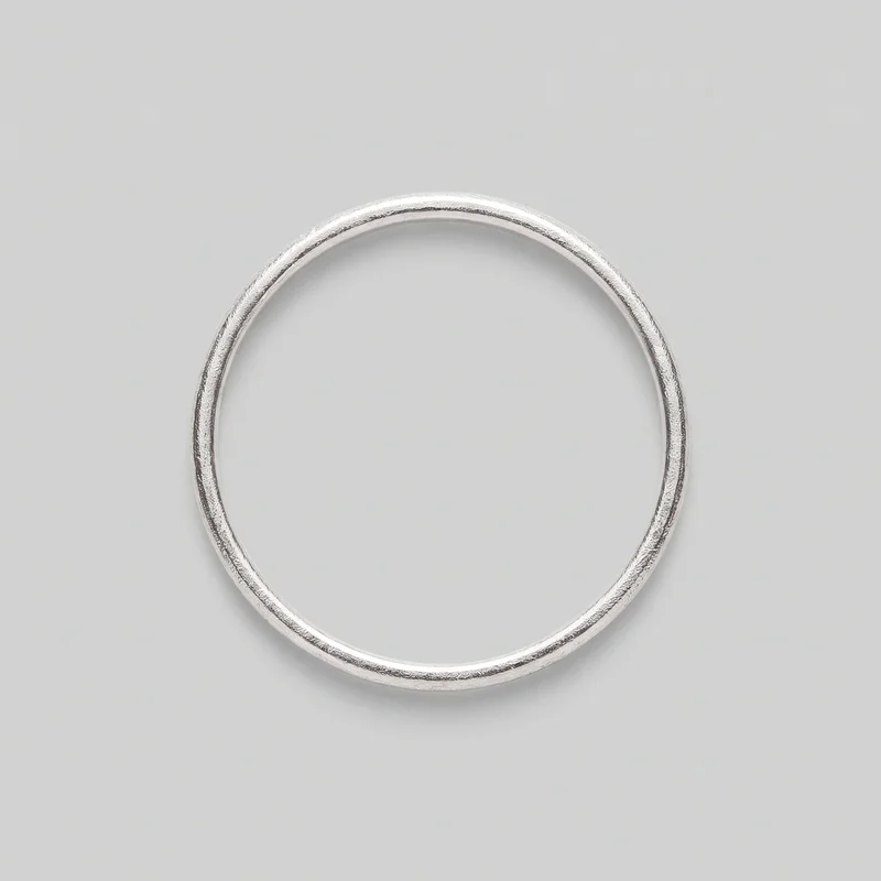 A complete silver stacking ring lies flat against the backdrop, viewed from above. The ring has a continuous circular band with an open center, a rounded domed outer profile, and a smooth inner edge. Subtle irregular etched or hammered-looking texture extends around the exterior, with no stones, settings, logos, prints, or other embellishments visible.