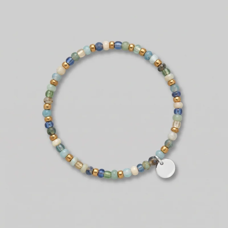 A complete women's beaded bracelet is laid in a circular shape. The strand combines rounded and short barrel-shaped beads with alternating smooth spacer beads and varied translucent, opaque, speckled, and striated finishes. A flat round disc charm hangs near the lower right from two visible jump rings, and no clasp is visible.