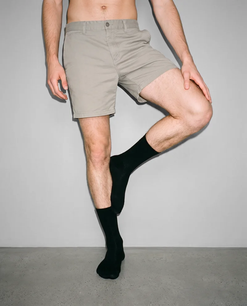 Black men's dress socks shown from the foot to calf in a front-view lower-body crop, against a pebble grey studio-wall backdrop.