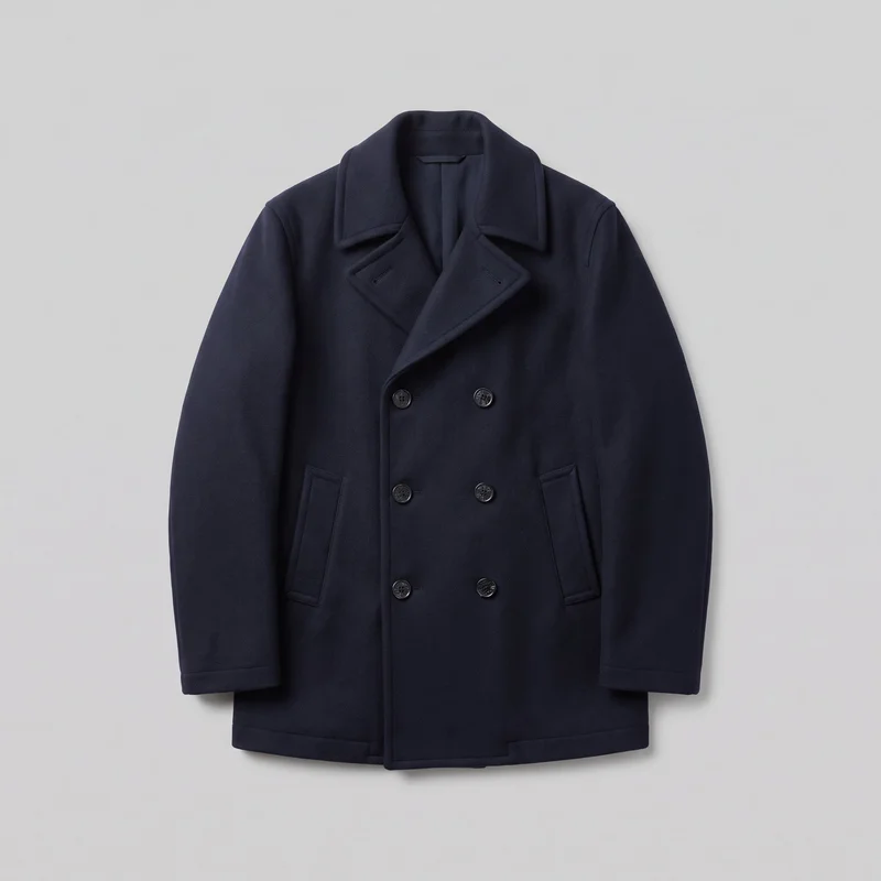 A men's navy wool peacoat is shown in a mostly complete front view against a plain backdrop. The coat has a structured regular silhouette, a wide notched lapel collar, long sleeves with plain cuffs, and a hip-length straight hem. Six visible round buttons form two vertical columns on the double-breasted front, with two angled welt pockets set low on the front.