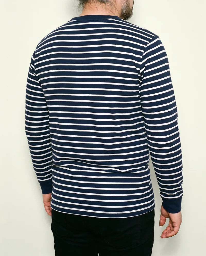 A male model wears a men's navy striped long-sleeve tee, shown from an angled rear view with his arms relaxed. The torso is framed against an ivory lace studio backdrop.