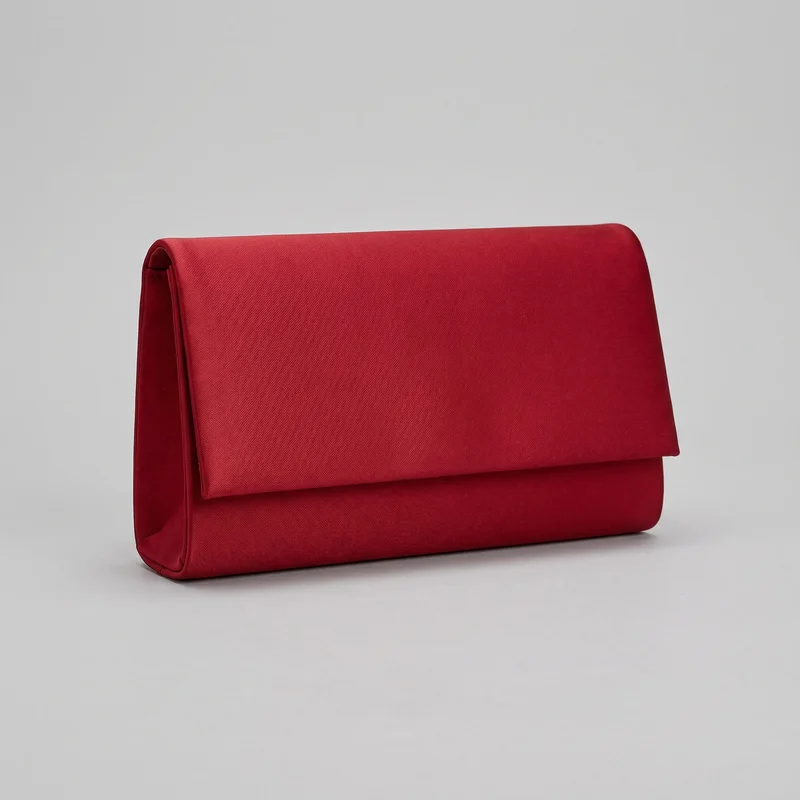 A red envelope-style clutch bag is shown as a standalone product, angled to reveal its fold-over front flap and left side gusset. It has a structured rectangular body, softly rounded flap corners, rounded boxed side and bottom edges, and raised piping or bound seams along the edges. No handle, strap, closure hardware, pockets, logo, print, or embellishment is visible.