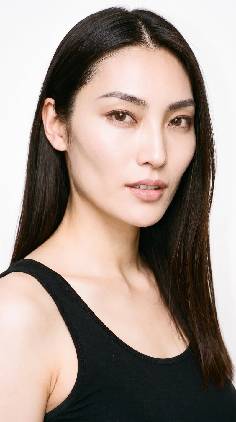 A 34-year-old Japanese woman with porcelain skin and a cool undertone has a diamond-shaped face, with a narrow forehead and jaw and cheekbones forming the widest part of her face. She has thick eyebrows, brown eyes, and thin lips. Her dark-brown hair is straight, smooth, and divided evenly at the centre.