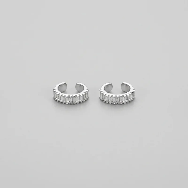 Two matching open-ended C-shaped ear cuffs are shown upright as a standalone product, viewed from a slightly elevated angle. Each cuff has a smooth rounded band, a row of vertical rectangular faceted stones along the lower front, evenly spaced prong-like notches across the upper rim, and small rounded bead settings along the bottom edge. The plain inner surfaces and open backs are visible.