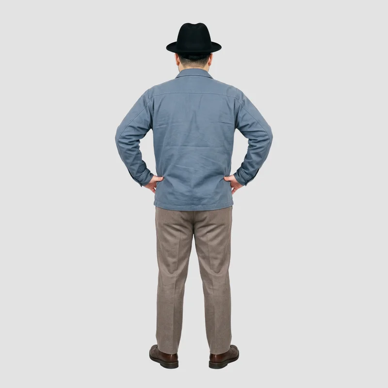 A 20-year-old Japanese male model wears a men's black wool fedora, shown from the back in a wide stance. The environmental framing places him against a flat fog-grey backdrop.