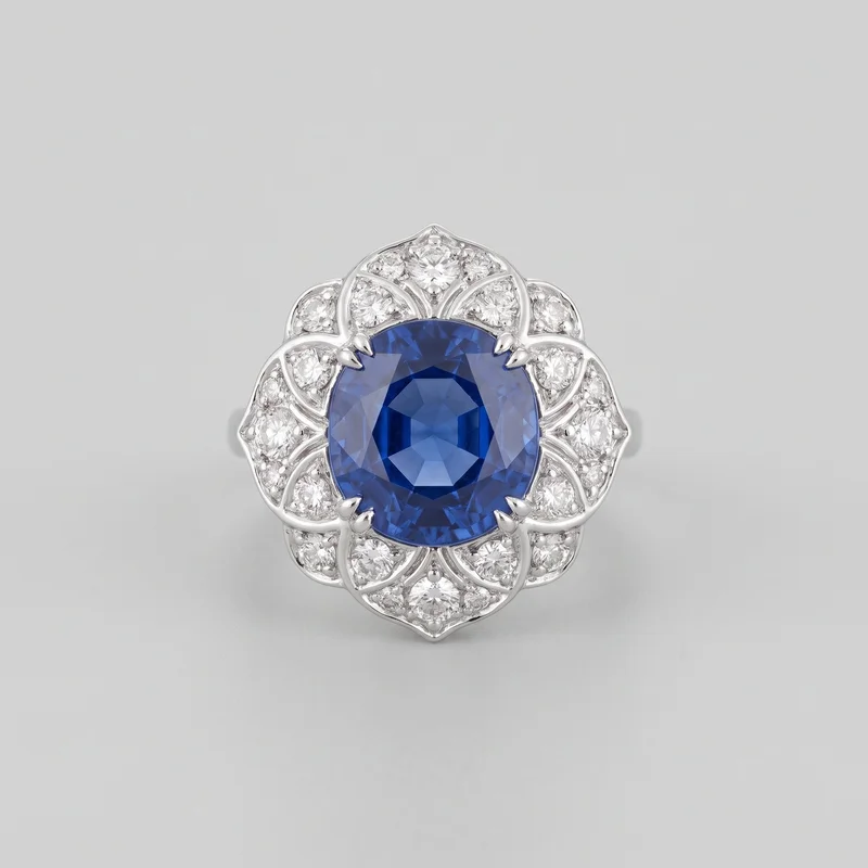 An ornate ring is shown in a close standalone front view. Its raised symmetrical face features an oval faceted center stone held by prongs, surrounded by a scalloped floral halo of petal-shaped openwork segments set with round faceted accent stones. Curved ribs, bead-like setting details, pointed top and bottom tips, and part of the band are visible at the sides.