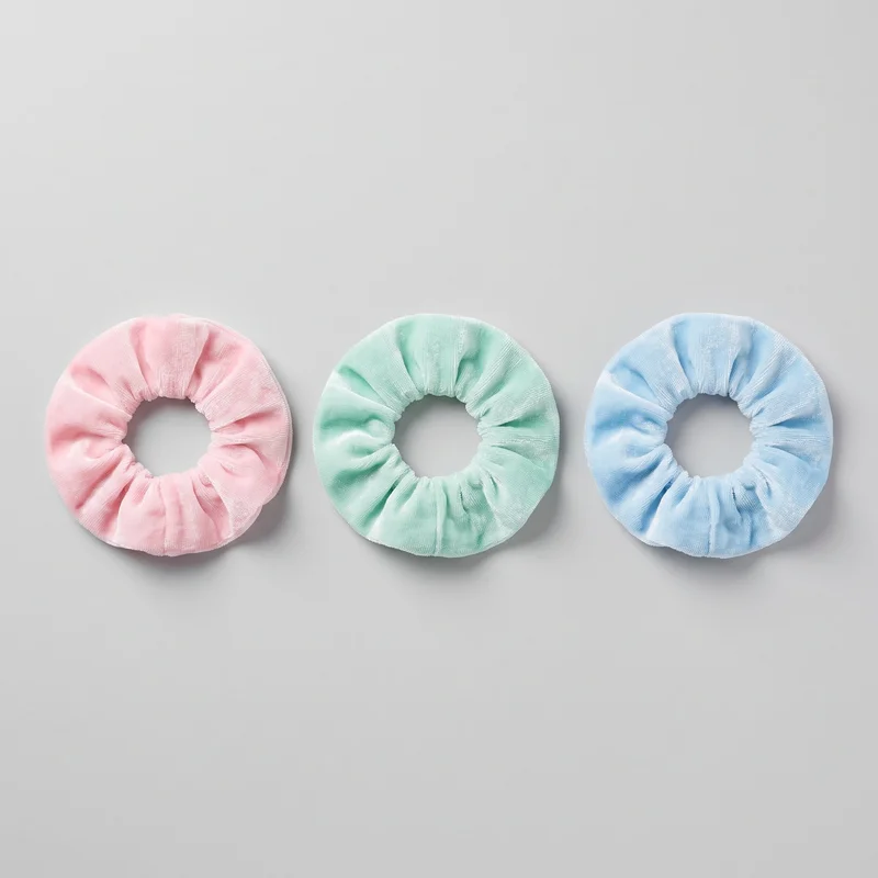 Three matching pastel scrunchie hair ties are laid side by side as a standalone product view. Each has a covered elastic core, gathered tubular outer fabric forming soft ruched folds, a rounded padded ring silhouette, and a clearly visible central opening with finished inner and outer edges. No logos, prints, patches, embroidery, or embellishments are visible.