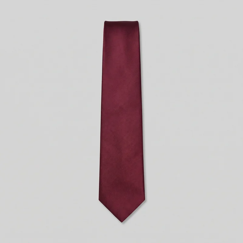 A single burgundy necktie lies flat in a centered view, showing its full blade and pointed triangular tip. The tie has a plain surface with a fine woven texture, clean edges, and a squared folded top end.