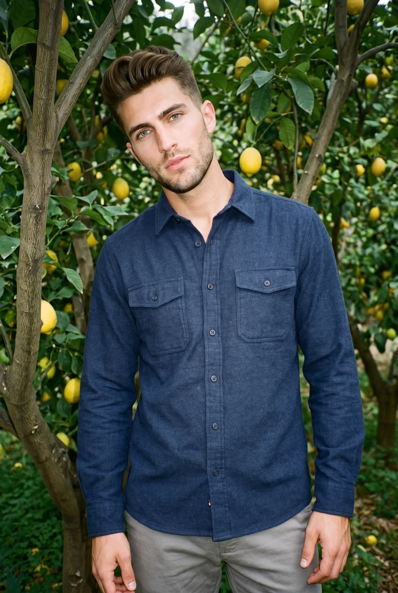 A 25-year-old Caucasian male model wears a navy flannel overshirt in an upper-body front view with a shoulder-drop pose and natural expression. A Lemon Orchard backdrop is visible behind him.