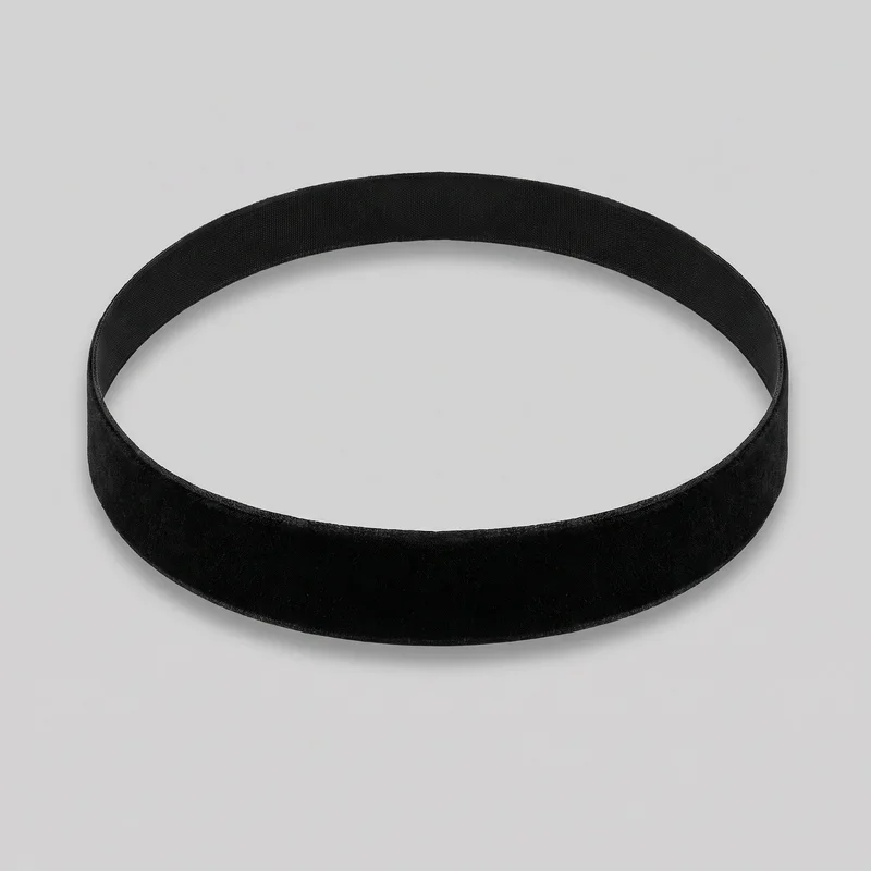A standalone black velvet choker is shown as a closed oval band on a plain surface. It has a broad, structured profile with smooth top and bottom edges, a soft-looking slightly plush exterior, and subtle edge binding.