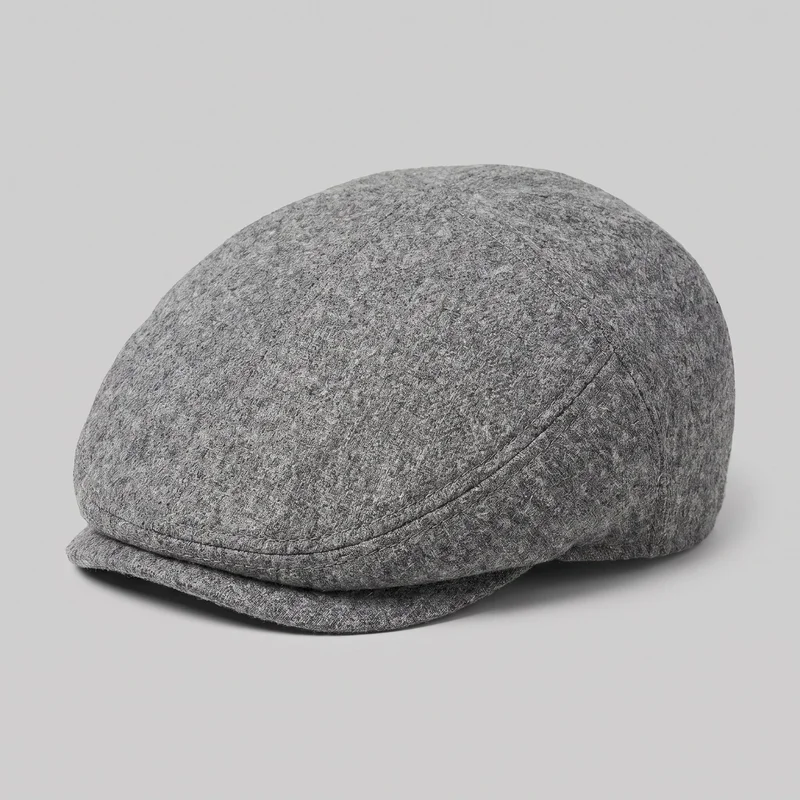 A standalone angled view of a men's grey wool flat cap with a low rounded crown, close-fitting silhouette, and short front brim tucked beneath the crown edge. Curved panel seams, a seam band above the brim, visible stitching, and an all-over mottled textured surface are shown; no closures, logos, prints, patches, embroidery, or embellishments are visible.