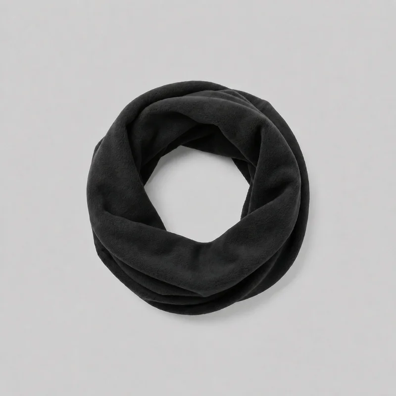 A black fleece neck gaiter is shown alone, coiled flat into a circular ring with an open center. Its continuous wide band has soft overlapping folds, rounded edges, and a smooth plush-looking surface; no closures, logos, prints, or embellishments are visible.