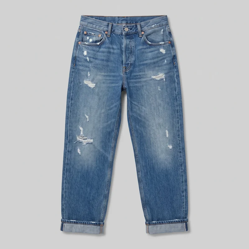 Women's distressed boyfriend-fit jeans shown in a complete front flat-lay view. The jeans have a relaxed mid-rise waistband, five-pocket styling, whiskering and fading, scattered abrasions and frayed torn patches on both front legs, and loose straight legs finished with broad single rolled cuffs.
