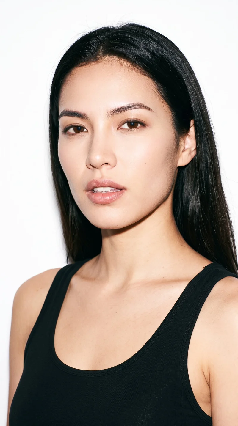 A 19-year-old Arab woman with medium skin and a warm golden undertone. Her face is angular, with sharp, defined cheekbones and jawline. She has medium-thick eyebrows, green eyes, and full lips. Her black hair is styled in soft waves.