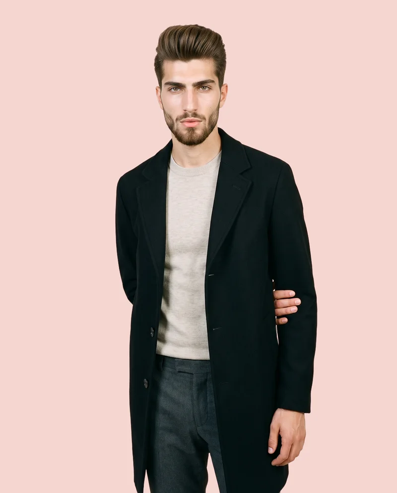 A 19-year-old Turkish man wears a men's black overcoat in a front-facing, three-quarter-length view. One elbow is positioned behind his back, and he has a soft facial expression. The image uses a flat-color Ballet Slipper backdrop.