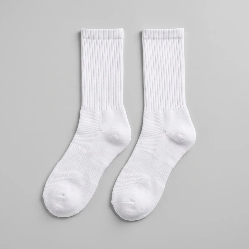 A pair of white crew-length sports socks is laid flat, showing the full thicker ribbed cuffs, vertically ribbed tube legs, shaped heels, and rounded closed toes. The foot areas have a denser knit with subtle reinforced-looking zones at the toes, heels, and arches. No logos, prints, closures, or embellishments are visible.