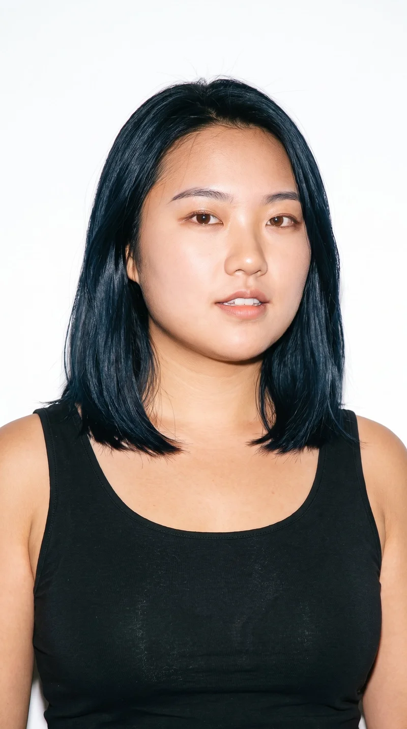 This 23-year-old Chinese woman has a light-tan complexion with a neutral undertone. Her face has soft, youthful features, full cheeks, and rounded contours. She has thin eyebrows, brown eyes, and thin lips. Her deep black hair is styled in a long bob that falls between her chin and shoulders.