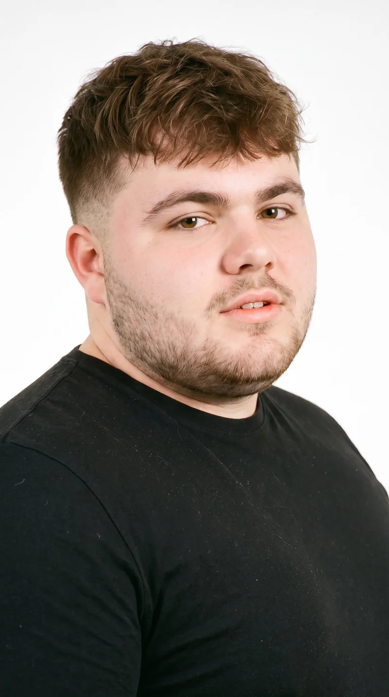 This 20-year-old Caucasian man has porcelain skin with a cool undertone and a round face defined by soft, full contours with few angles. His eyebrows are medium in thickness, and his eyes are brown. He has thin lips and brown hair styled in a short textured crop with layered texture on top and closely cut sides. Very short facial-hair growth creates a faint, even shadow across the beard area.