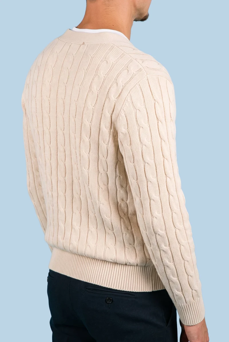 A male model is shown from the torso in an angled rear view, wearing a men's cream cable-knit cardigan with his arms relaxed. The cardigan is presented against a flat pale aqua backdrop.
