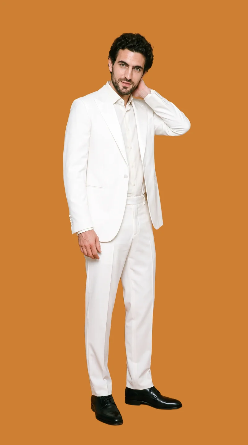 A 33-year-old Caucasian man wears a white dinner-jacket tuxedo in a full-body front three-quarter view. He poses with one hand behind his neck and a confident expression against a flat bronze backdrop.
