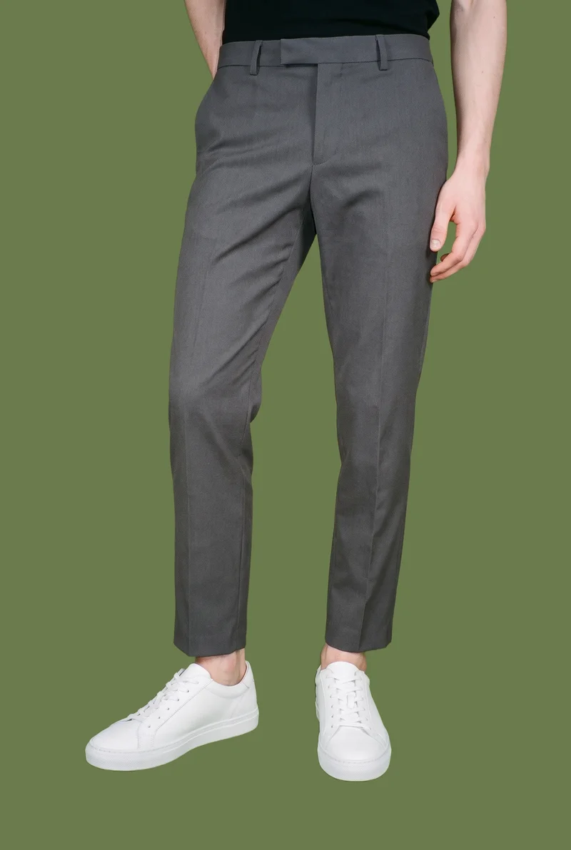 Men's white leather sneakers shown in a front view, with one foot positioned forward. The shoes are framed in a lower-body composition against an olive-green flat-color backdrop.
