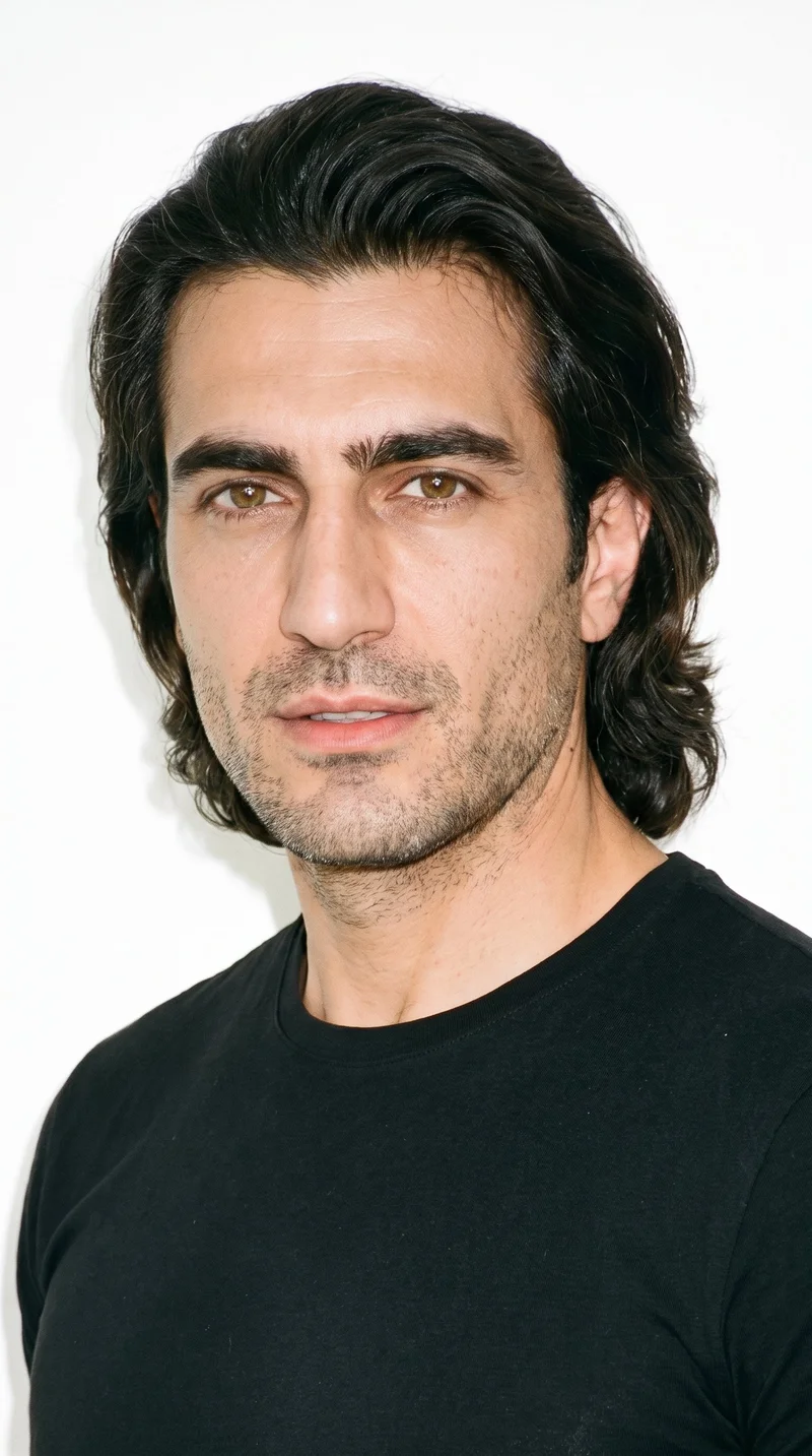 A 46-year-old Turkish man with lightly tanned skin and a warm golden undertone has a Roman face shape with strong classical features, a prominent nose line, and a defined jaw. His thick eyebrows frame brown eyes, and he has full lips. His dark-brown hair is medium to long, brushed back with body and movement extending past the ears, while fine, closely trimmed stubble lightly covers the beard area.