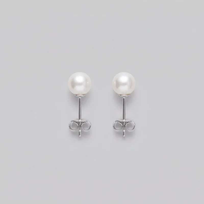 A complete pair of women's pearl stud earrings is shown as a standalone product. Each earring has a smooth round bead front in a small cup-like setting, a straight post stem, and a symmetrical double-loop butterfly clutch back.