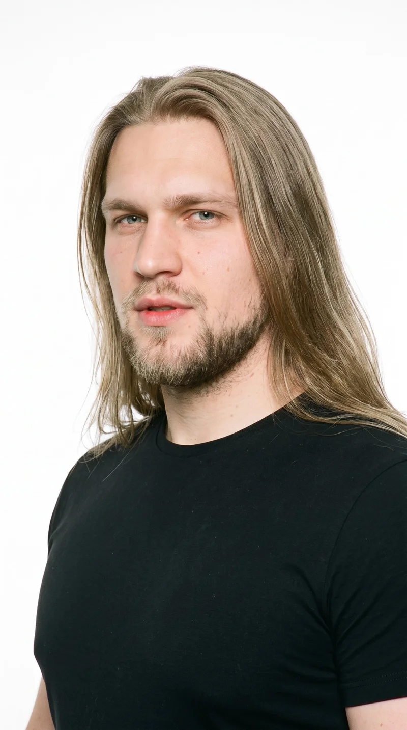 A 27-year-old Slavic man with fair skin and a neutral undertone has a rugged, weathered face with a heavy jaw. His medium-thickness eyebrows frame cool grey eyes, and he has medium-sized lips. His darker, muted blonde hair is long, worn loose past the shoulders, and naturally voluminous. A short, structured boxed beard follows the cheeks and jaw with defined edges.
