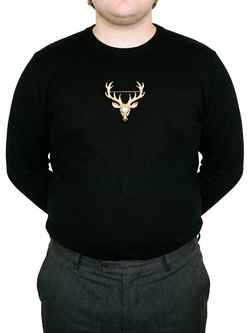 A men's gold brooch shown on a male torso in a front view, with the hands positioned behind the back. The brooch is presented against a pure white backdrop.