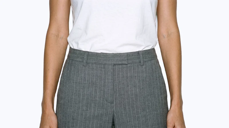 Grey pinstripe suit trousers shown from the front, framed from the hips with the hips level against a porcelain-colored flat backdrop.