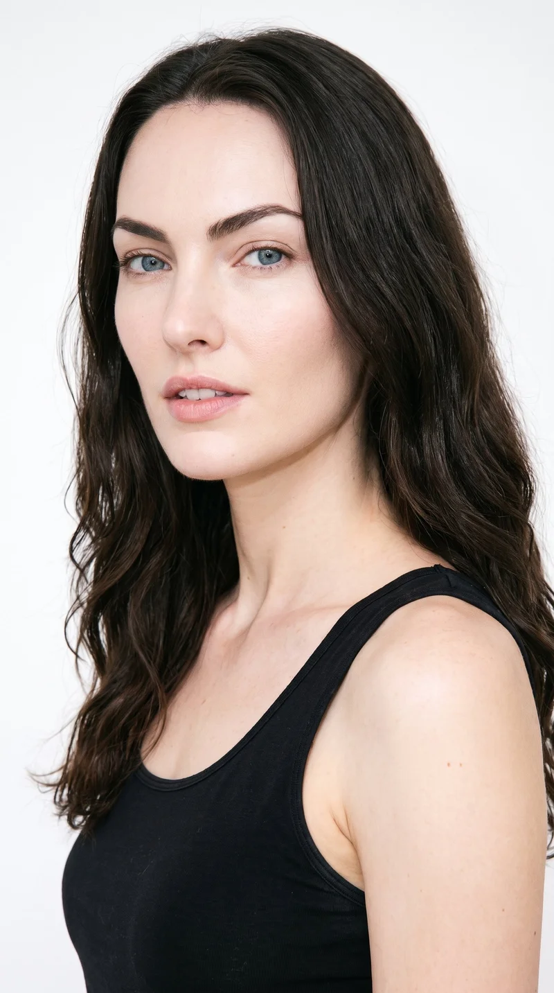 This 25-year-old Caucasian woman has lightly tanned fair skin with a cool undertone. Her heart-shaped face has a wider forehead that narrows to a more pointed chin. She has thick eyebrows, blue eyes with a cool undertone, and thin lips. Her long dark-brown hair is worn loose past the shoulders with natural volume.