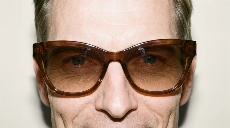 Brown cat-eye sunglasses shown from the front at eye level against an alabaster studio-wall backdrop.