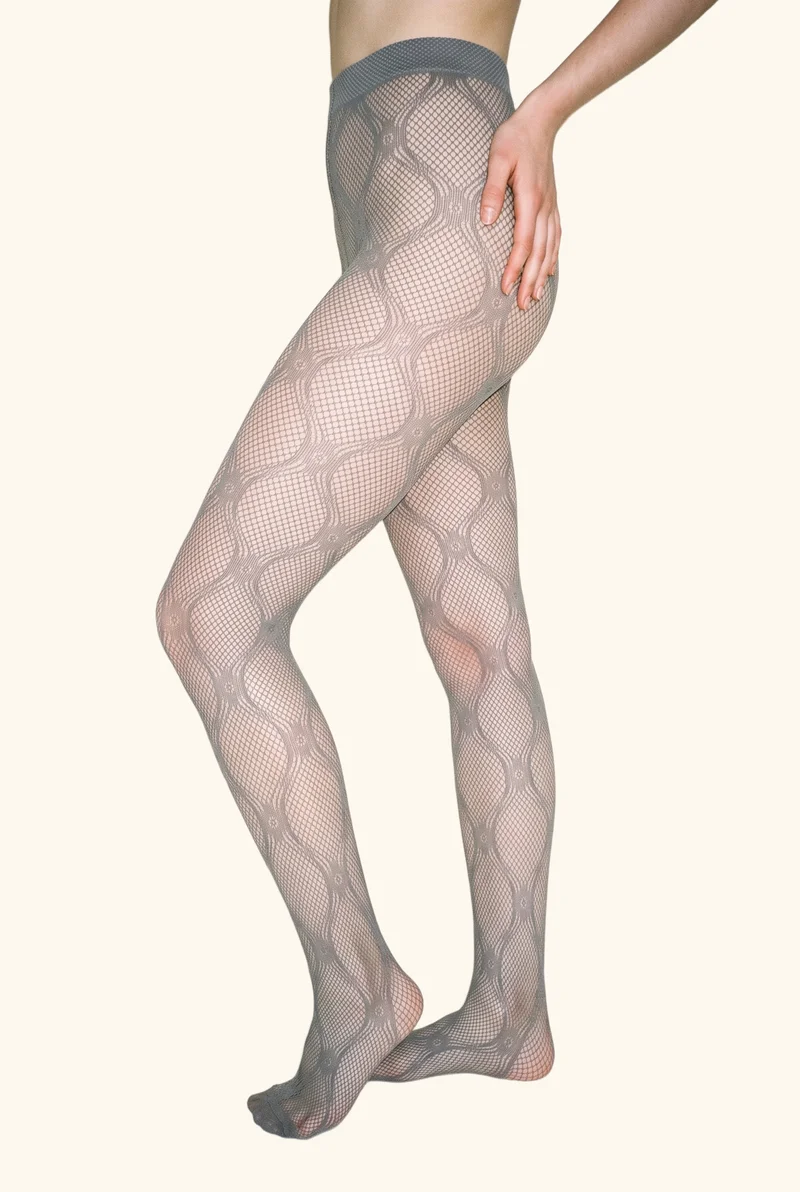 A lower-body side view shows a person wearing patterned fishnet tights with their knees turned inward. The tights are presented against a creamy white flat-color backdrop.