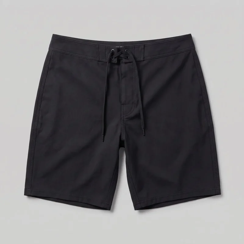 Black board shorts shown in a flat standalone front view. The shorts have a relaxed straight-leg silhouette, mid-rise fixed waistband, long length, straight hem openings, a lace-up drawstring closure through paired waistband grommets, hanging cord ends, a covered center fly panel, reinforced waistband panels, stitched side panels, and double-stitched seams.