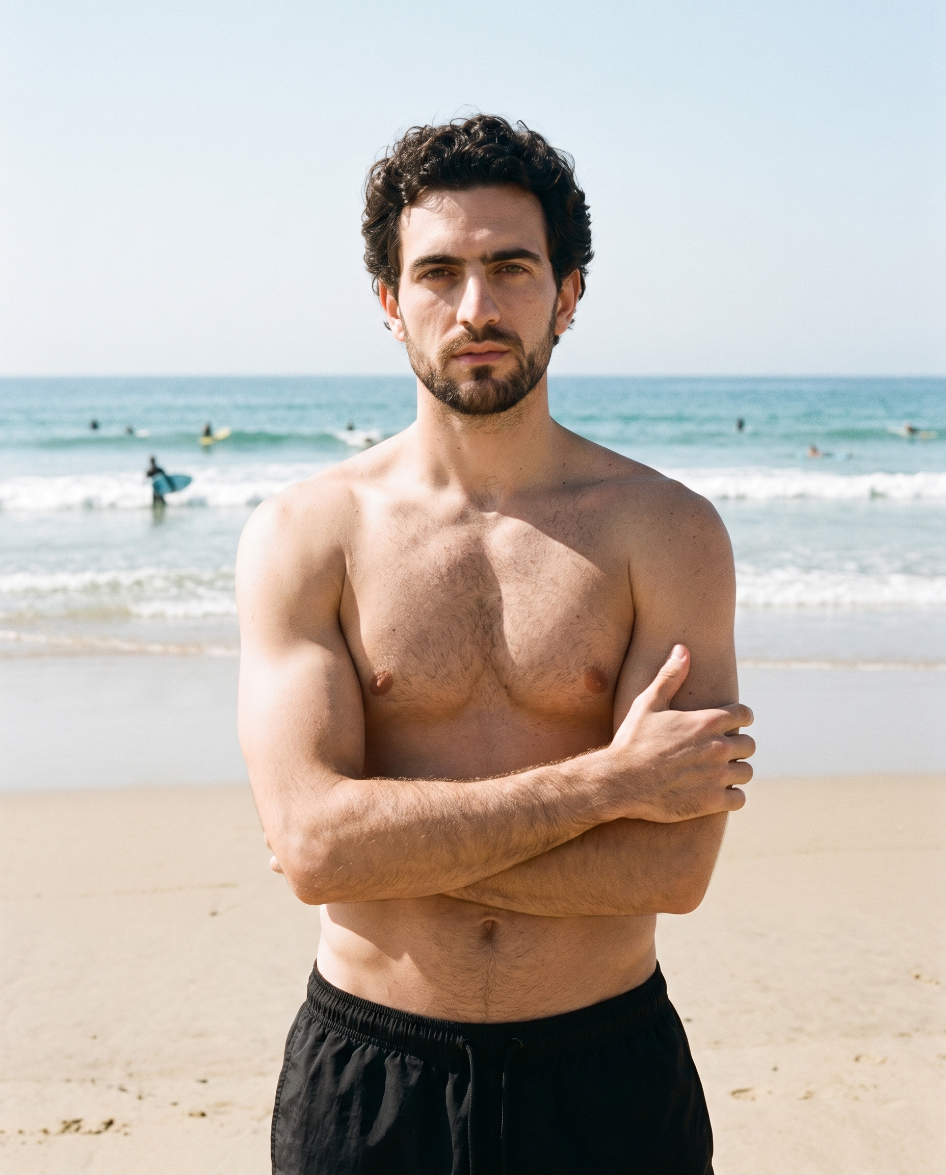 A 33-year-old Caucasian man is shown from the front in an upper-body view, wearing black swim trunks with his arms crossed and a confident expression. A surfing beach backdrop is visible behind him.