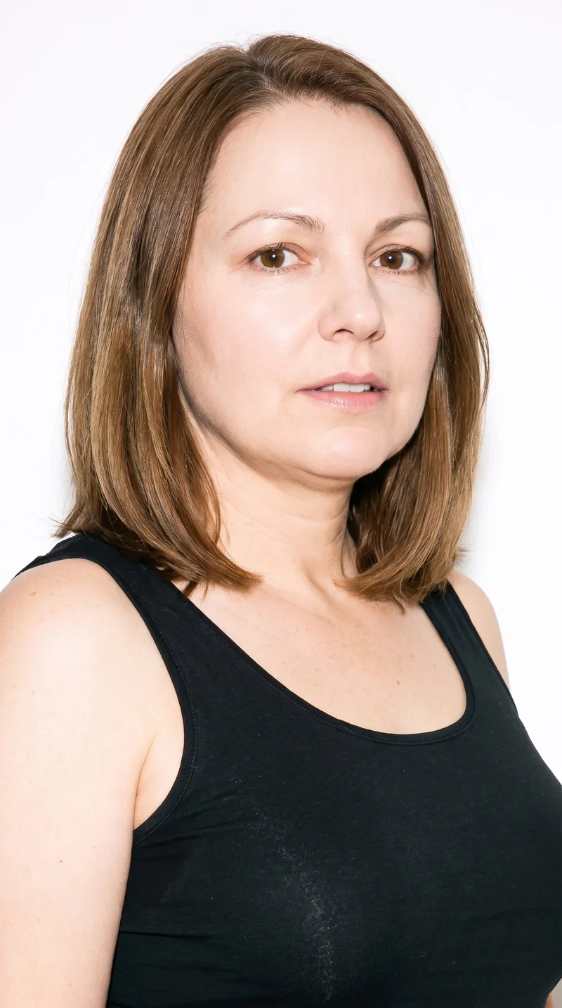 A 51-year-old Caucasian woman with porcelain skin and a warm golden undertone has an oval face with balanced proportions and a softly rounded jaw. She has thin eyebrows, medium lips, brown eyes, and brown hair styled in a long bob that falls between the chin and shoulders.