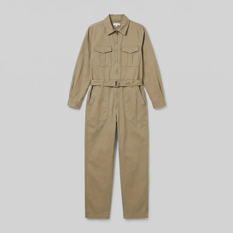 A complete front-facing view of a khaki utility-style women's boilersuit laid flat. It has a point collar, long sleeves with straight cuffs, a full-length front zipper, shoulder yoke seams, two chest patch pockets with pointed flaps and pleated panels, angled lower patch pockets, belt loops, and a matching waist belt with a double D-ring buckle. The garment has straight pant legs, plain hems, and visible topstitching throughout.