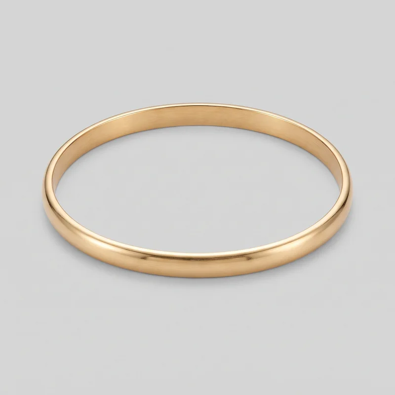 A complete gold bangle bracelet is shown alone at a slight angle, revealing its continuous seamless circular band, open center, smooth rounded outer face, raised rounded rim edges, and flatter inner wall. The rigid bangle has no visible closure, hinge, clasp, logo, print, stones, engraving, or other embellishments.