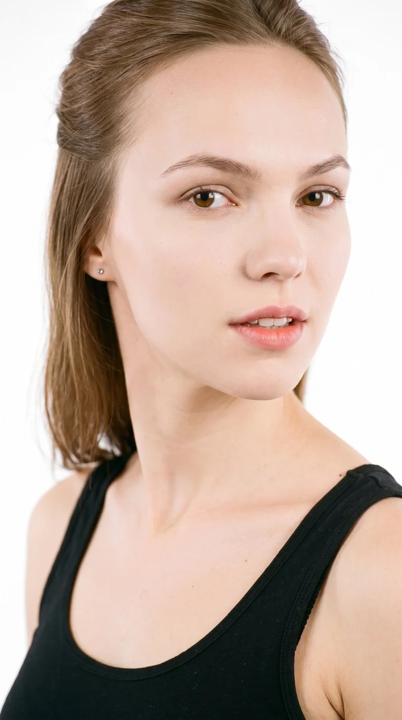 This 23-year-old Caucasian woman has very pale skin with a cool undertone and a heart-shaped face, with a wider forehead narrowing to a more pointed chin. She has thin eyebrows, blue eyes with a cool undertone, and medium-sized lips. Her light-brown hair is styled half up and half down, with the upper section pulled back and the lower lengths hanging loose.