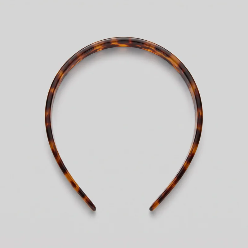A complete rigid U-shaped hair headband lies flat, viewed from above. It has a smooth arched band, rounded tips, a domed outer surface, slight tapering toward both ends, and an all-over mottled tortoiseshell-effect exterior.