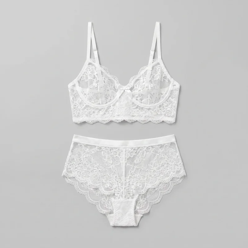 A matching white bridal lingerie set is arranged in a flat lay, with the lace underwire bra positioned above the high-waist brief. The bra features sheer floral lace, scalloped upper cup edges and hem, adjustable shoulder straps, a low center gore with a bow, and a wide longline-style lower band. The brief has a smooth high-rise waistband, sheer floral lace panels, a central front seam, scalloped leg openings and hem edges, and a narrower opaque gusset panel.