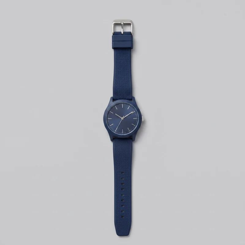 A complete women's navy rubber-strap sports watch is laid flat in a straight vertical orientation. The round case has a slim bezel, straight lugs, and a right-side crown; the dial features simple baton hour markers, fine minute ticks, and three slim hands without numerals or a date window. The strap has a raised pebbled texture, adjustment holes, keeper loops, and a rounded rectangular pin buckle.