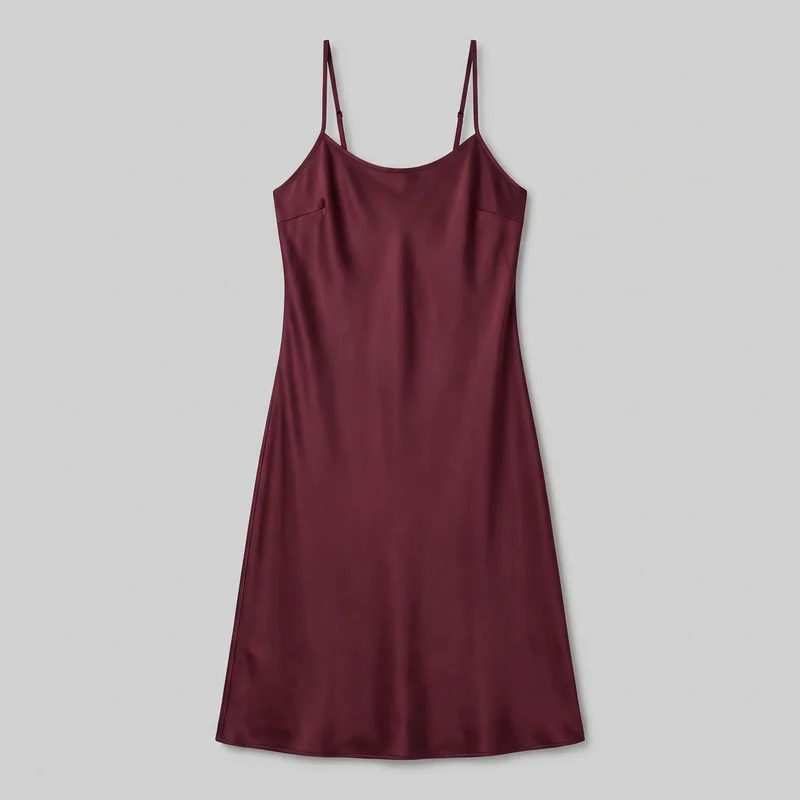 A burgundy women's slip dress is shown laid flat in a complete standalone front view. It has a scoop neckline, narrow spaghetti straps with visible adjusters, a sleeveless open-shoulder cut, angled bust seams, vertical side seams, a bodice-skimming silhouette, a slight A-line skirt, and a clean straight hem.